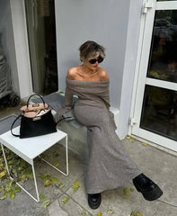 Woman in gray off-shoulder outfit sitting on a chair with a black handbag next to her.