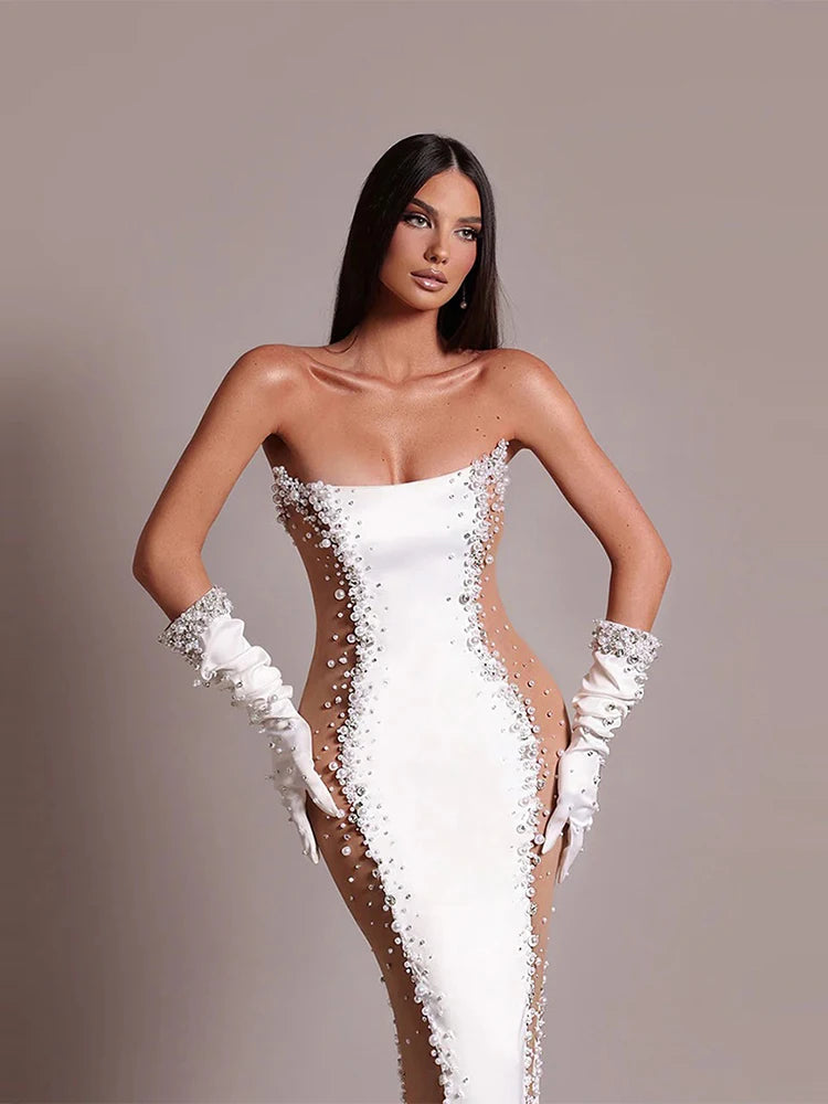 Woman wearing a white strapless gown with floral details and white gloves on a plain background