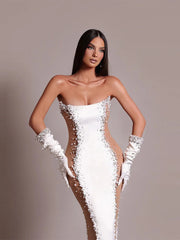 Woman wearing a white strapless gown with floral details and white gloves on a plain background