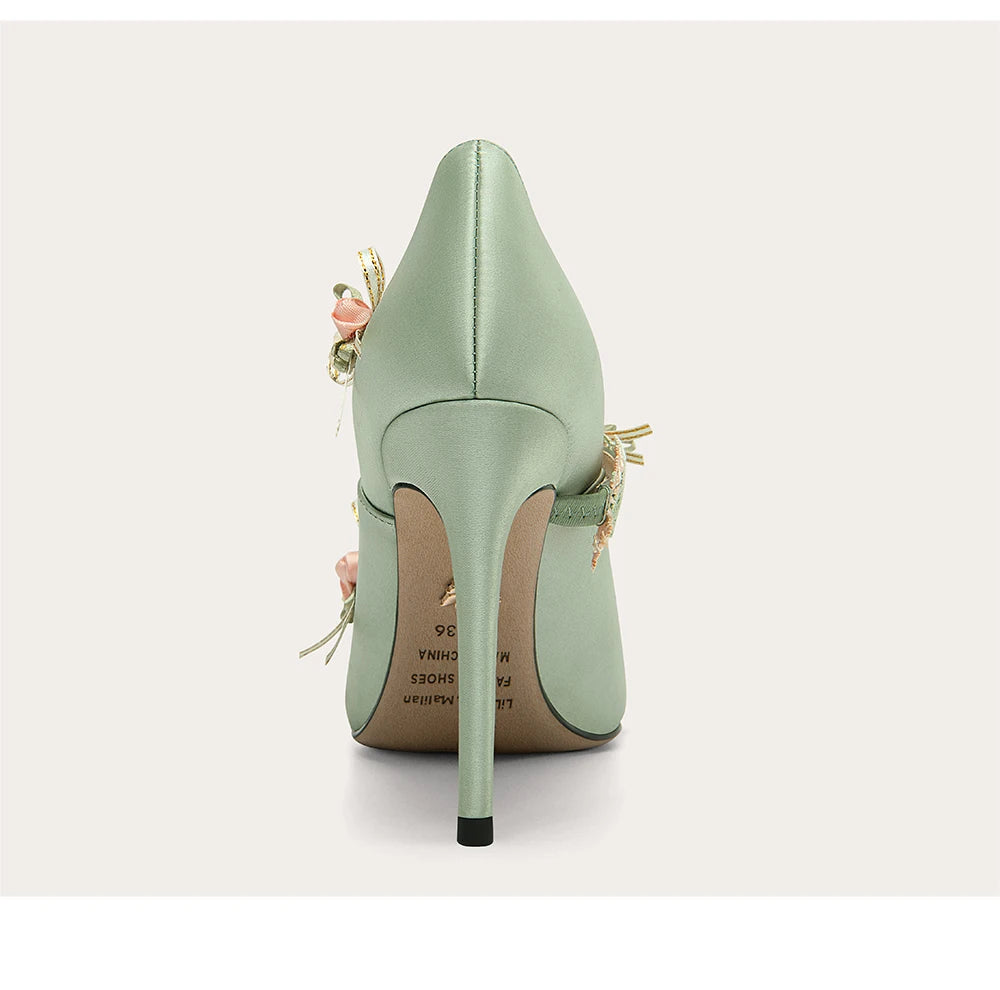 Mint green high-heeled shoe with floral details on a light gray background