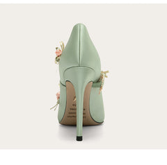 Mint green high-heeled shoe with floral details on a light gray background