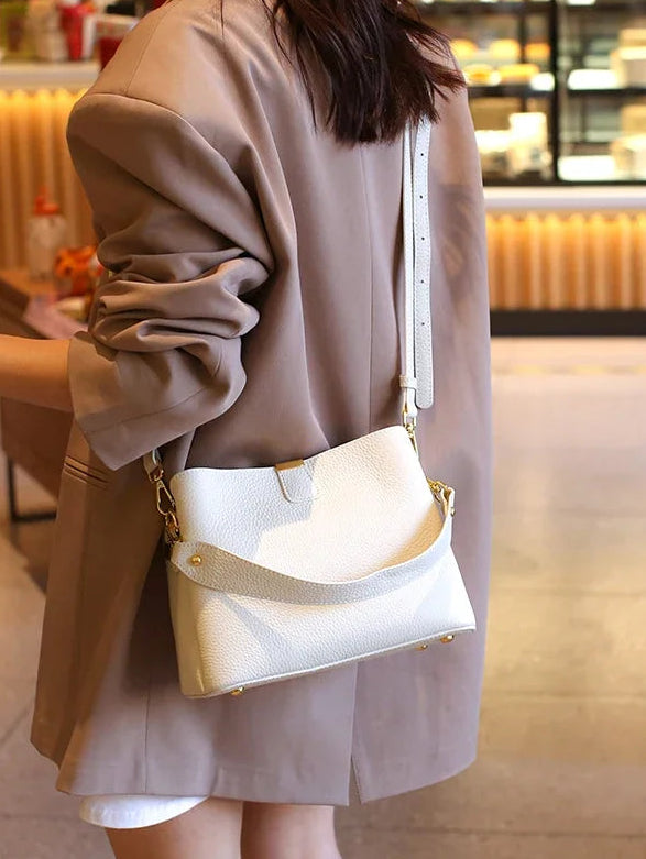 Person wearing a beige coat and holding a white handbag in an indoor setting.