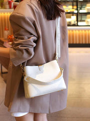 Person wearing a beige coat and holding a white handbag in an indoor setting.
