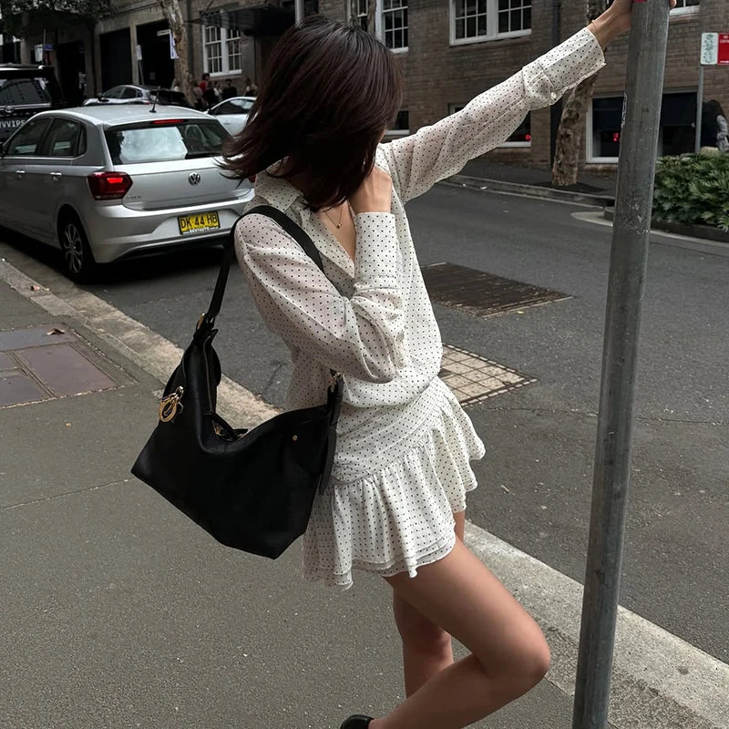 Woman in a white dress with a black handbag standing on a street corner.