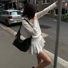 Woman in a white dress with a black handbag standing on a street corner.