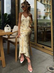 Woman in a yellow floral dress sitting outdoors at a cafe.
