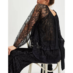Person wearing a black lace outfit sitting on a white stool against a white background