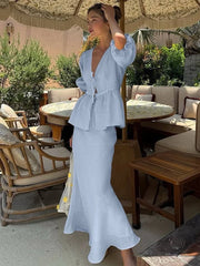 Woman in a light blue dress standing in an outdoor setting with tables and chairs.