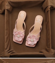 Pair of pink high-heeled sandals with floral decorations on a brown fabric background