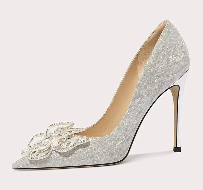 Silver high-heeled shoe with decorative bow on a light gray background