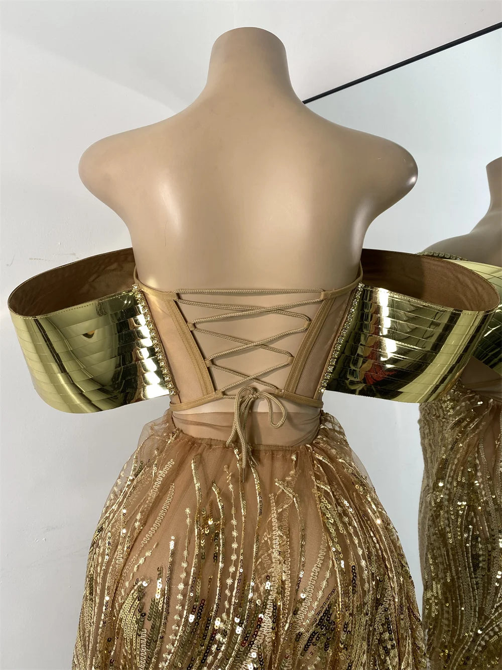 Mannequin wearing a gold and beige dress with metallic sleeves against a white background