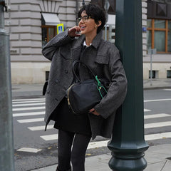 Woman in a gray coat leaning against a street lamp on a city street