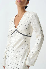 White dress with black polka dots and lace trim on a plain background