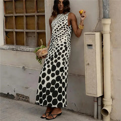 Woman in a polka dot dress standing against a wall with a window in the background.
