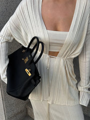 Person wearing a white outfit holding a black handbag with a gold clasp.