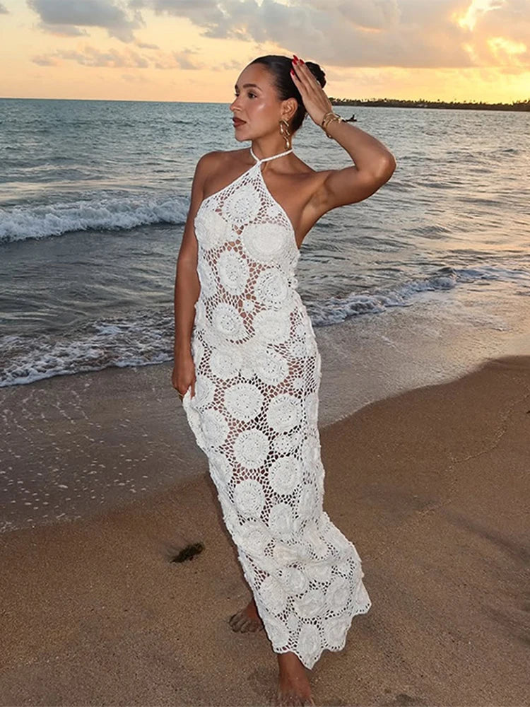 Woman in a white lace dress standing on a beach at sunset.