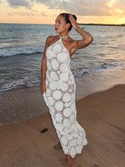 Woman in a white lace dress standing on a beach at sunset.