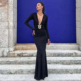 Woman in a black evening gown standing on stone steps with a blue wall behind her