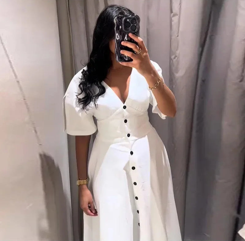 Woman wearing a white dress with black buttons in front of a neutral background