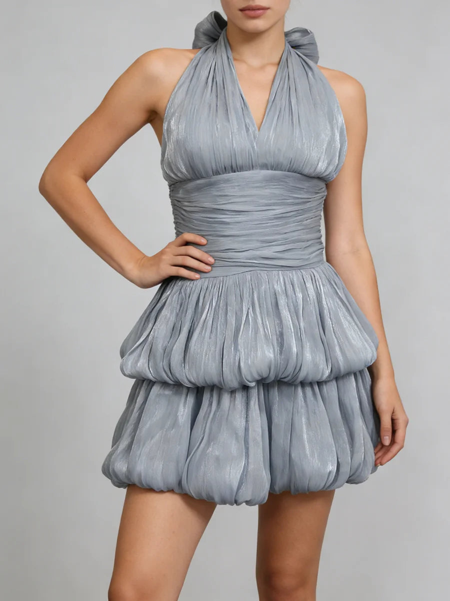 A woman wearing a blue pleated dress against a plain background