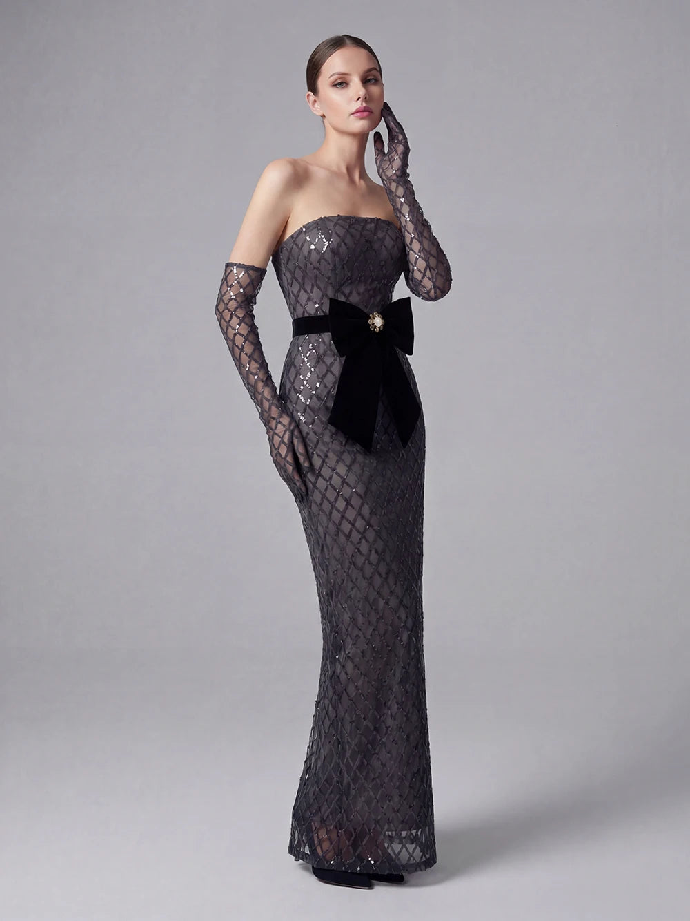 Woman wearing a black lace evening gown with a bow on a gray background
