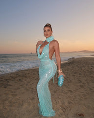 Woman in a turquoise dress standing on a beach at sunset