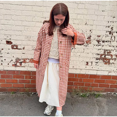 Person wearing a red and white checkered coat against a brick wall.