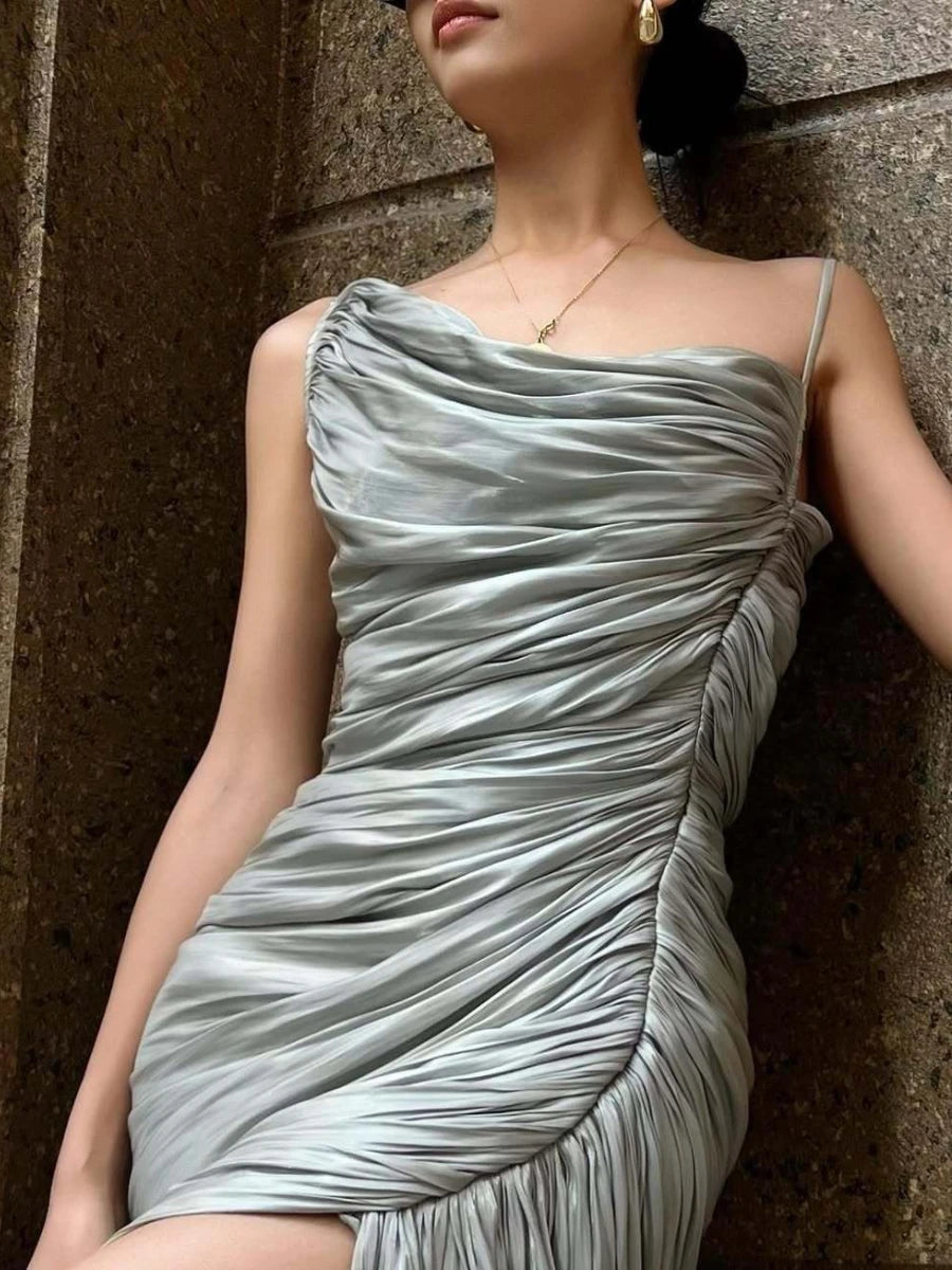 Woman wearing a silver one-shoulder dress against a textured wall.