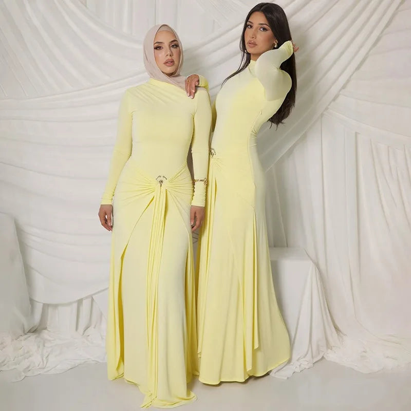 Two women wearing matching yellow long-sleeve dresses against a white draped curtain background.