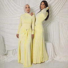 Two women wearing matching yellow long-sleeve dresses against a white draped curtain background.