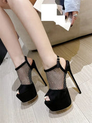 Black high-heeled shoes with mesh design worn by a person on a light wooden floor.