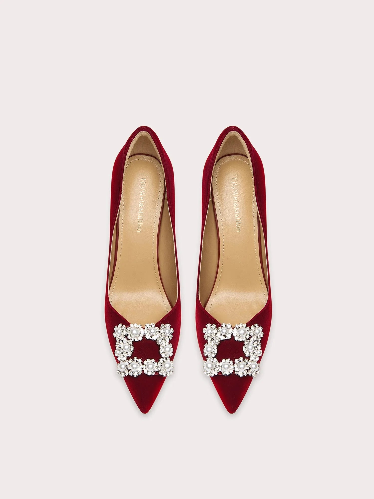 Red high-heeled shoes with pearl embellishments on a light gray background