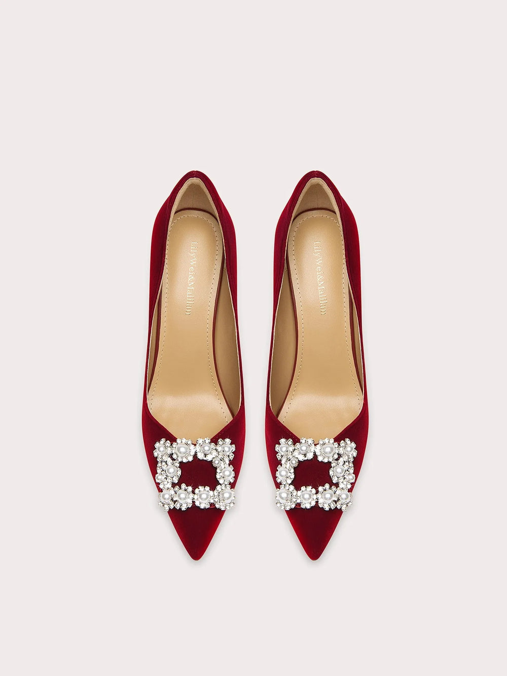 Red high-heeled shoes with pearl embellishments on a light gray background