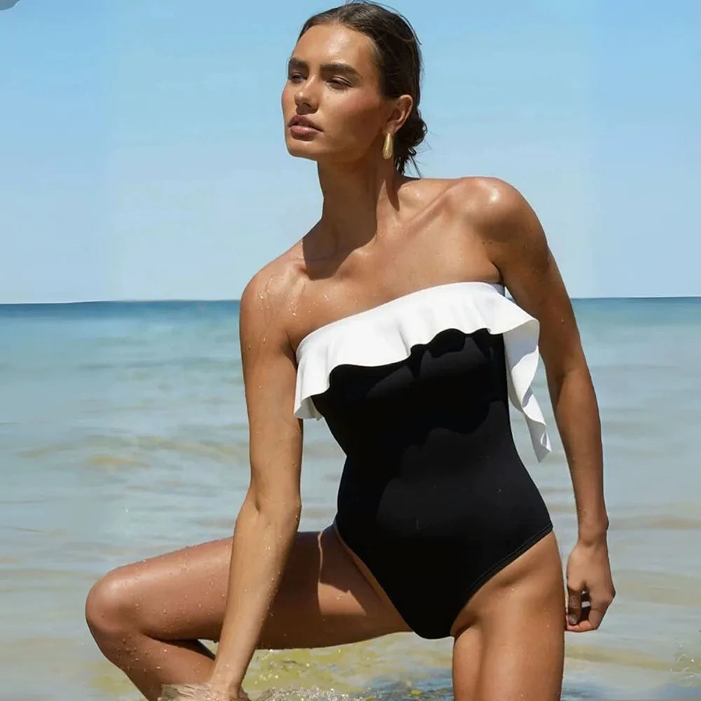 Model in a black and white ruffle monokini kneeling in the shallow ocean water.