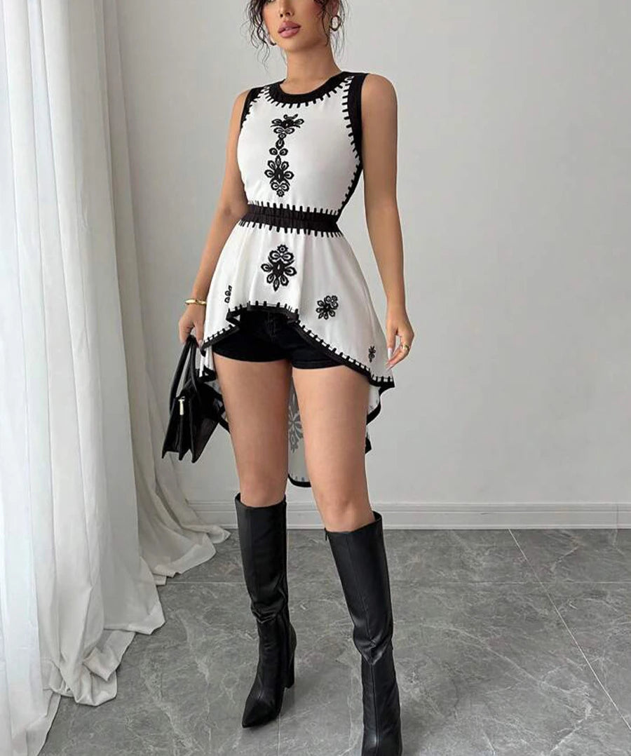 Woman wearing a black and white dress with floral patterns and black knee-high boots in a room.