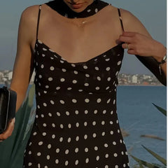Woman wearing a black polka dot dress by a body of water.