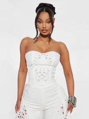 Woman wearing a white strapless outfit with intricate detailing on a plain background