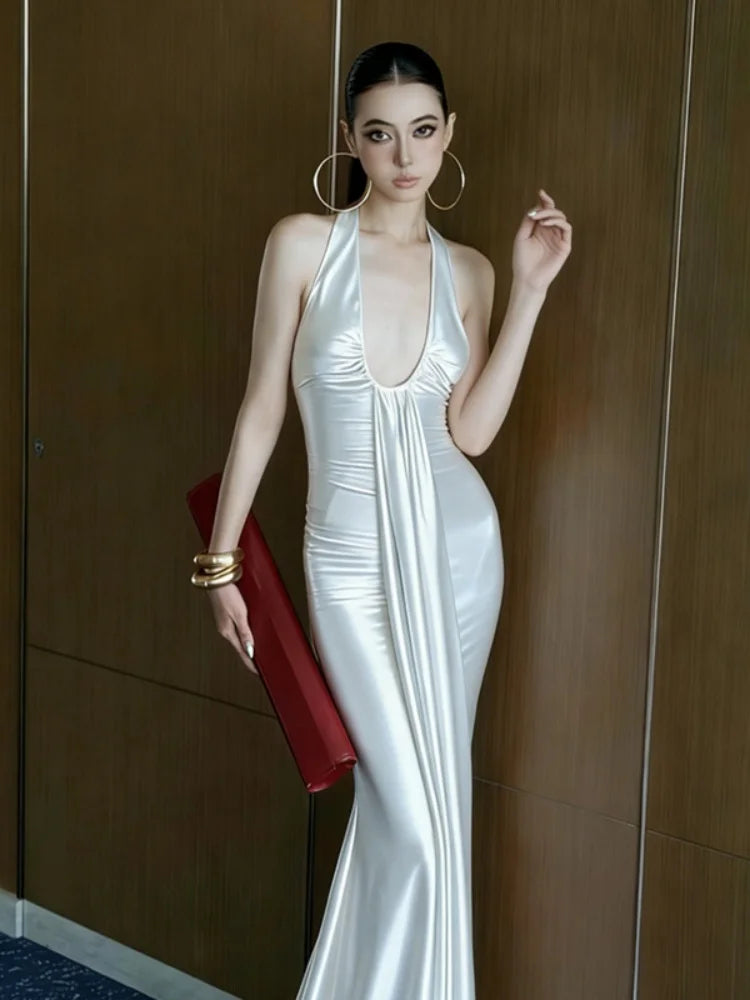 Woman in a white evening gown holding a red clutch against a wooden wall.