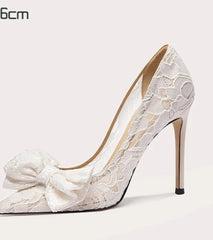 White lace high-heeled shoe with a bow on a light gray background