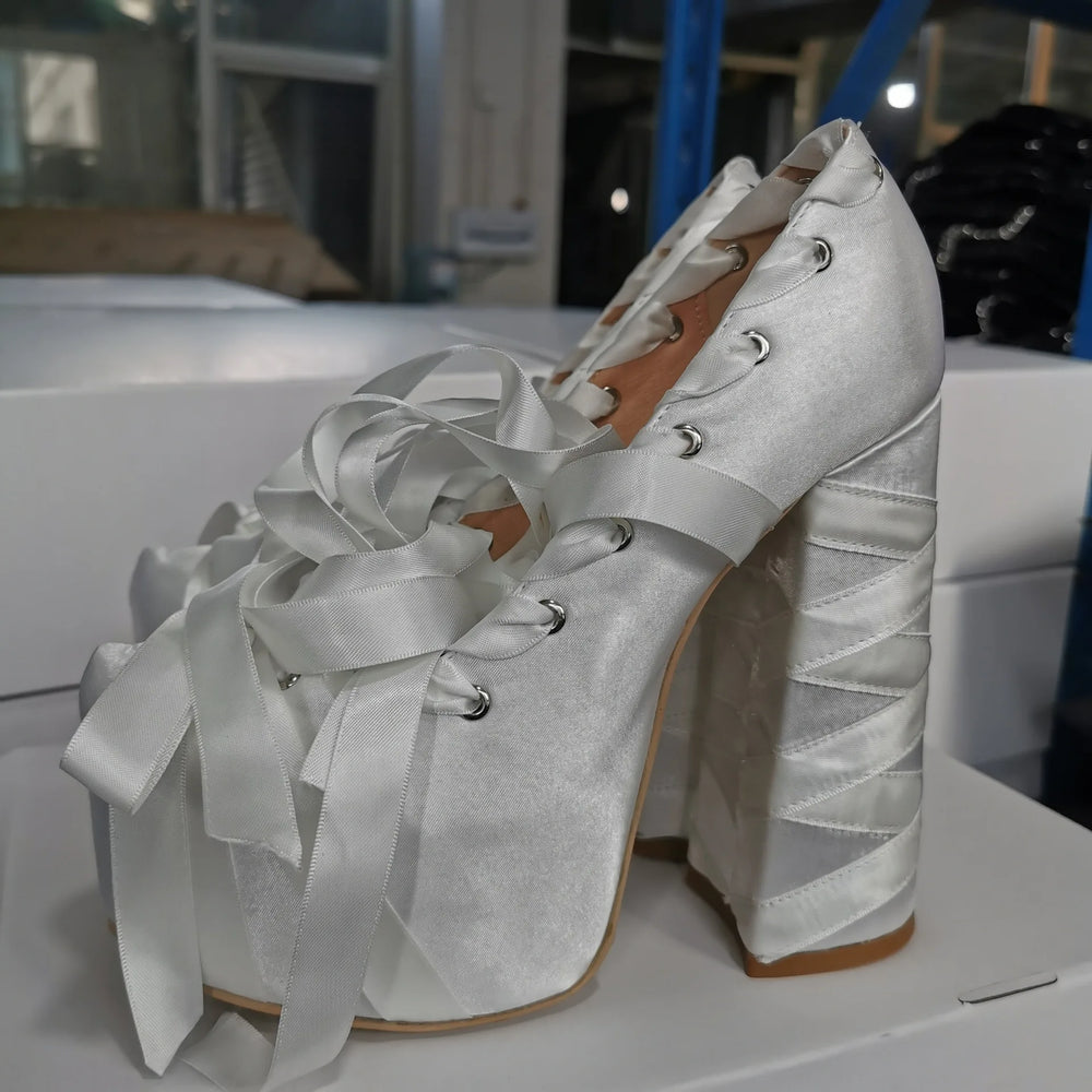 White satin high-heeled shoes with ribbons on a white surface.