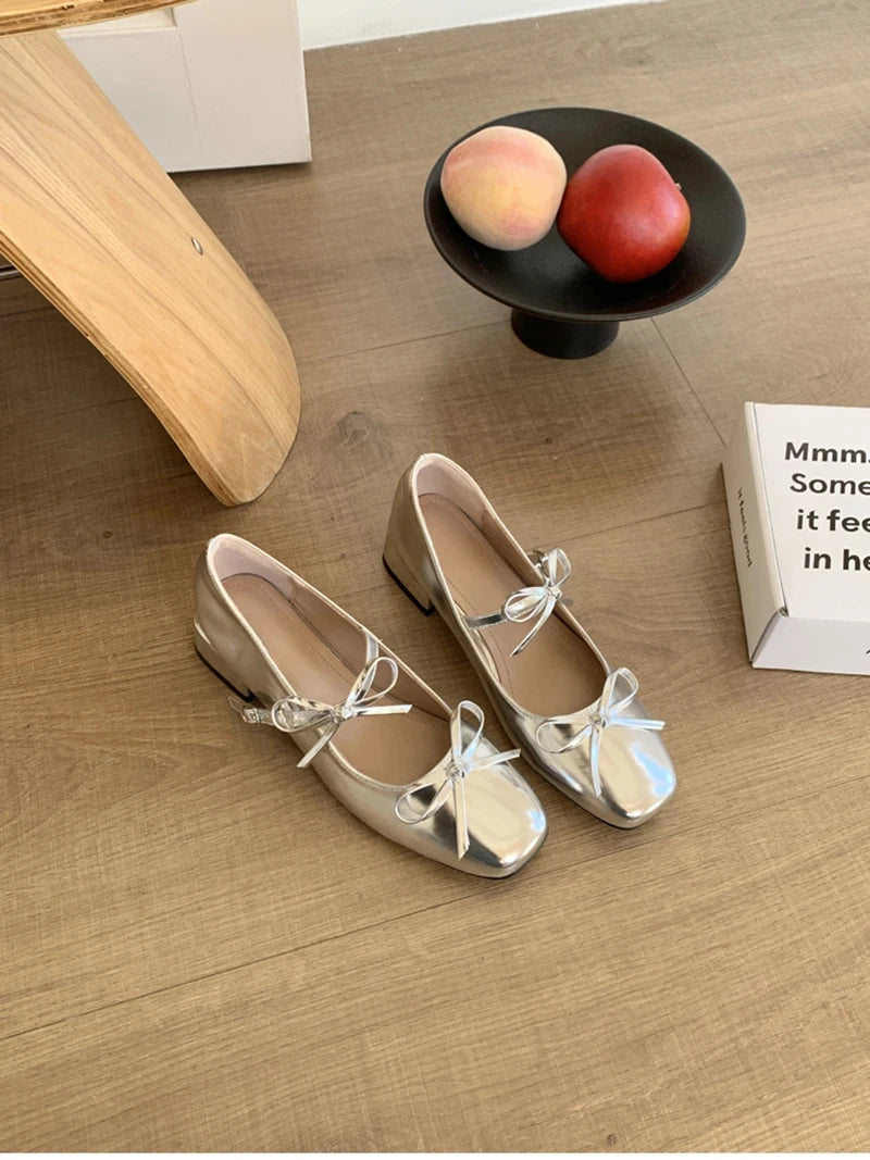 Pair of beige shoes with bow details on a wooden floor.