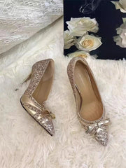 Pair of glittery high-heeled shoes with a bow on a textured white surface.