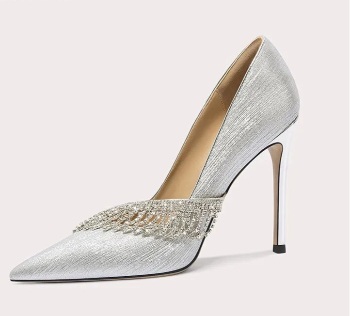 Silver high-heeled shoe with embellishments on a light gray background