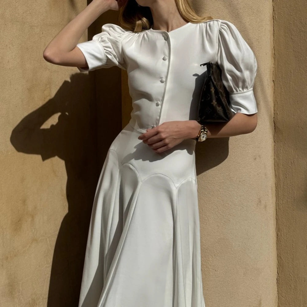 Woman in a white dress standing against a beige wall
