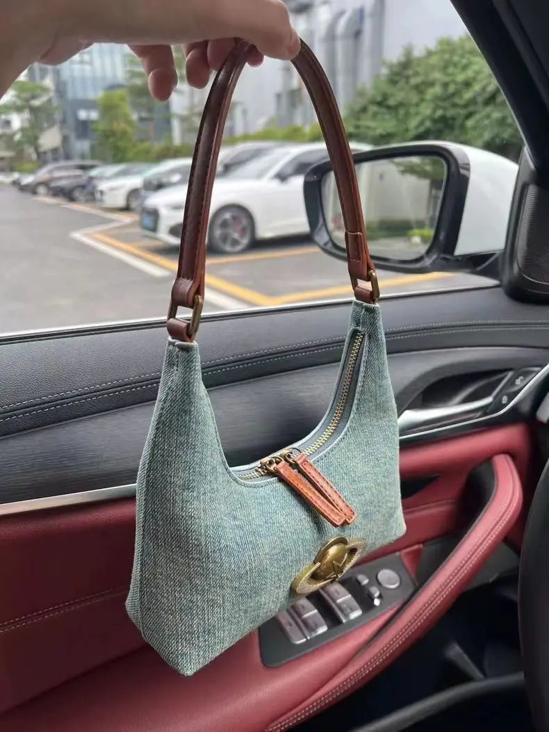 Green handbag with brown handle held inside a car.