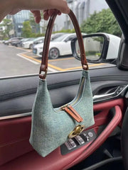 Green handbag with brown handle held inside a car.
