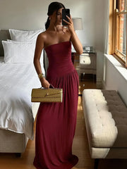 Woman in a burgundy dress holding a gold handbag in a bedroom.