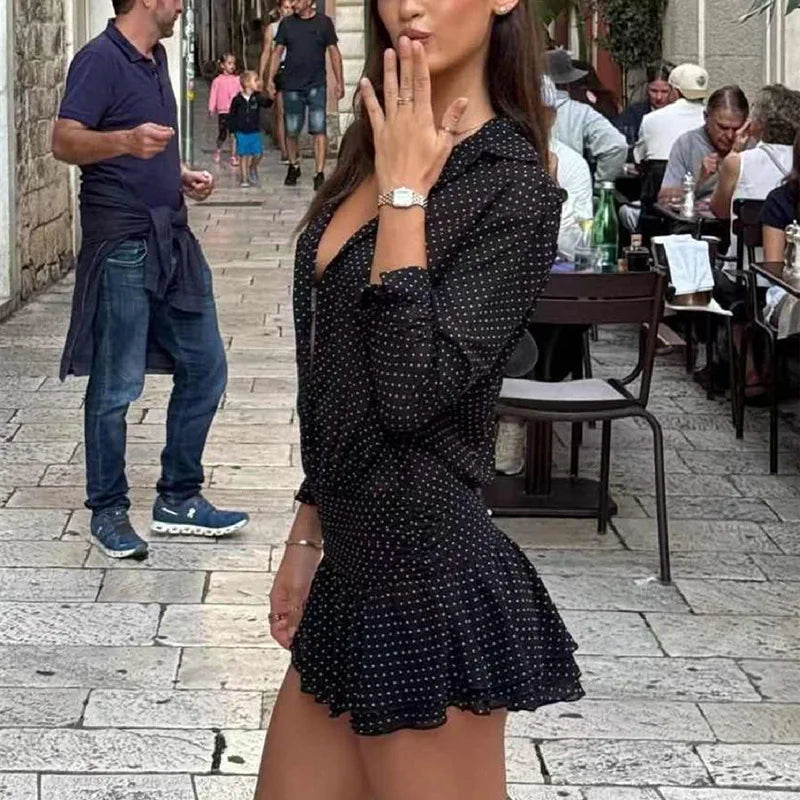 Woman in a black polka dot dress standing on a street with people in the background