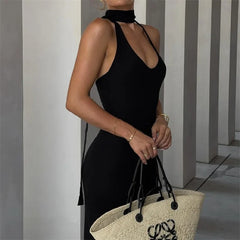 Woman in a black dress holding a straw bag with a brand logo against a striped wall.