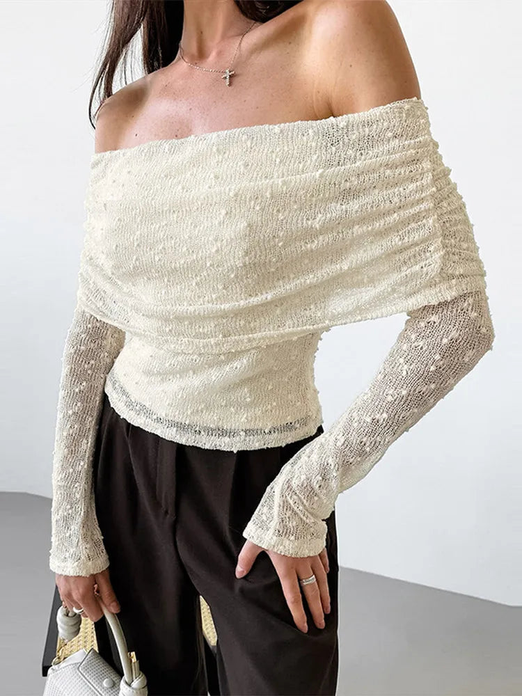 Person wearing a white off-shoulder textured top with black pants against a plain background